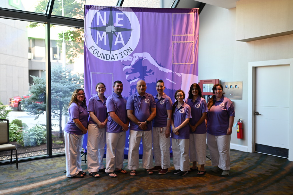 New England Martial Arts Foundation group wearing purple shirts in front of a NEMA Foundation banner