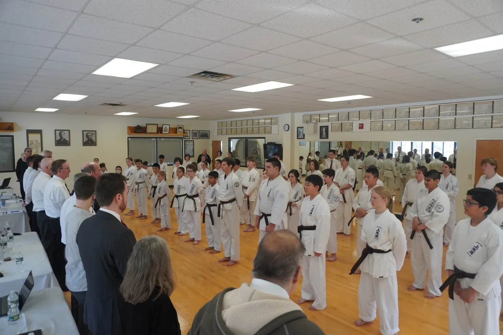 Black belt candidates gathered before senior judges in a dojo